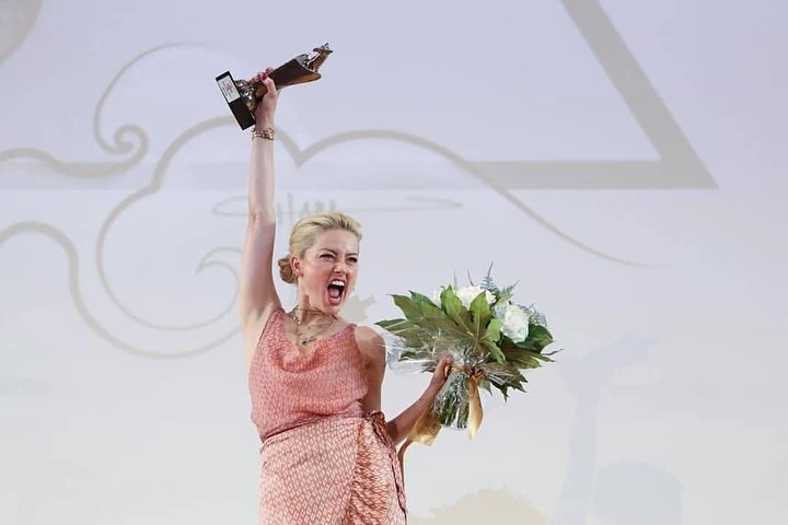 Amber Heard holding flower bouquet in left hand and upholding the award in her right hand