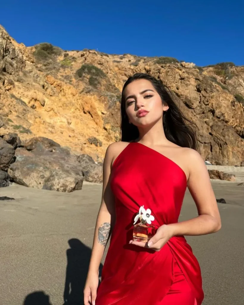 Isabela Moner wearing a red sleeveless dress and holding a flower in her hand